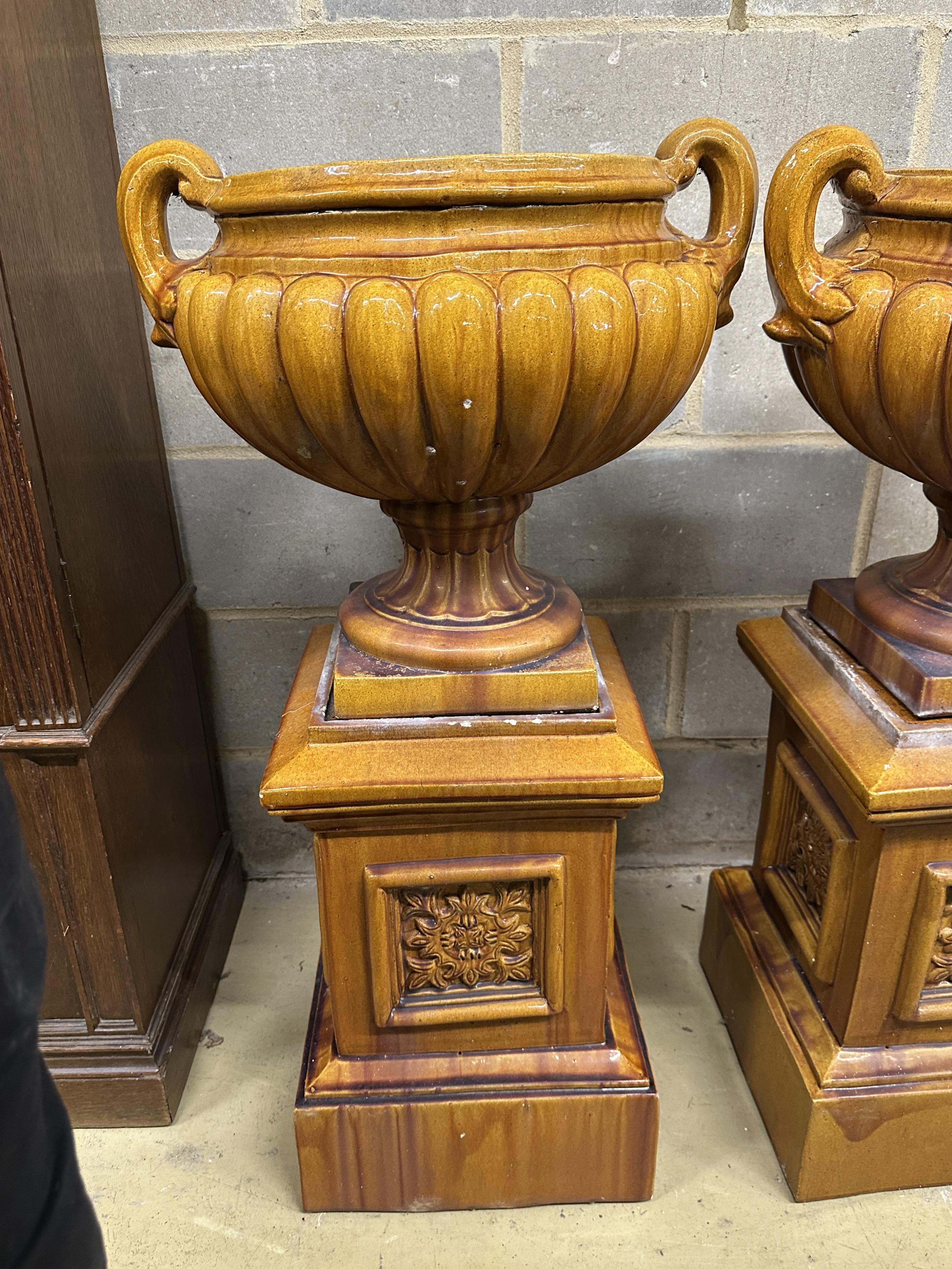 A pair of Victorian treacle glazed earthenware twin handled urns on square stands, height 104cm. Condition - fair, some losses to plinths